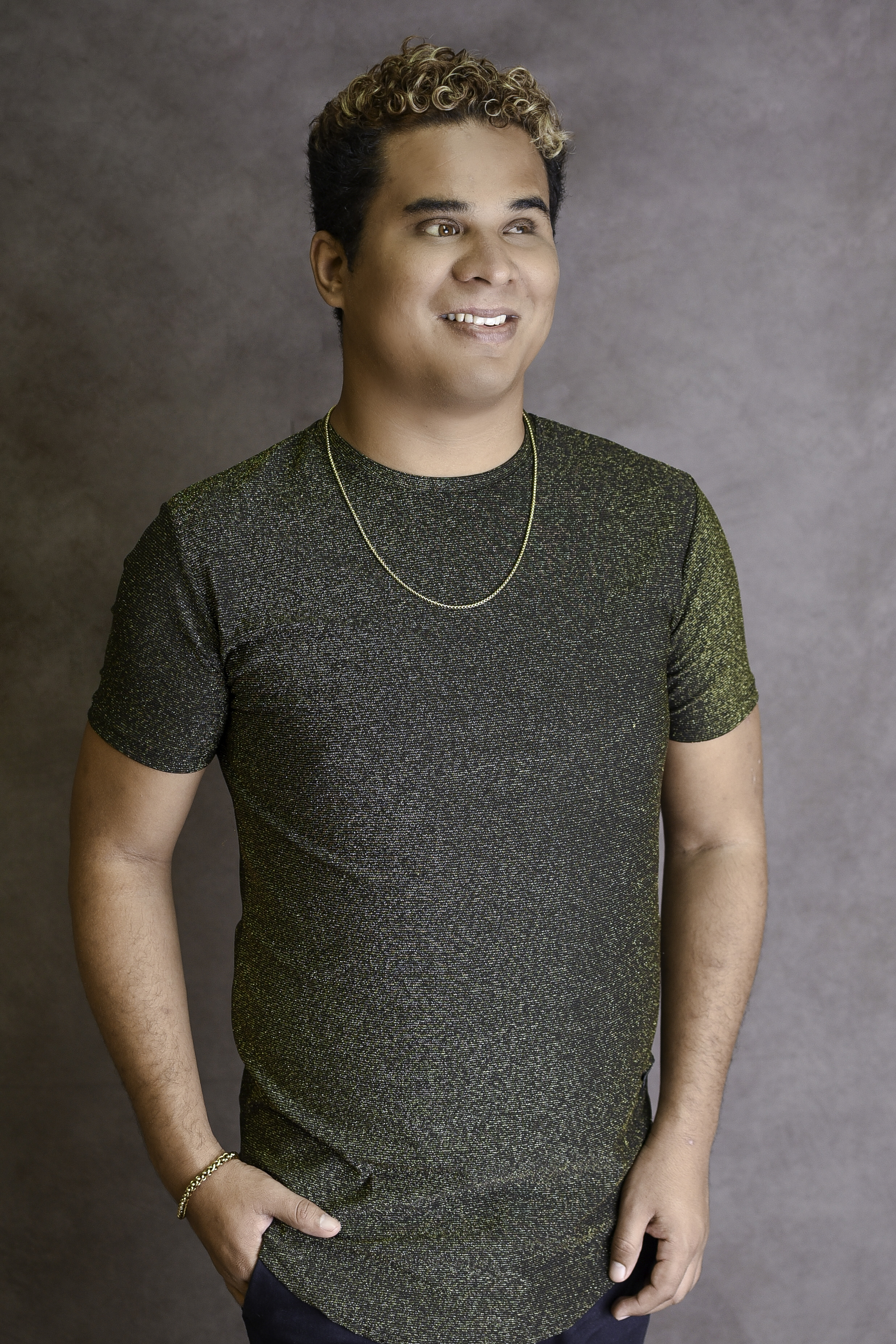 David Meireles sorrindo, usando camiseta verde, corrente dourada e cabelo cacheado